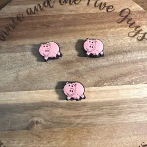 Three pink pig stickers laid out on a wooden surface with cursive text partially visible around the edge.