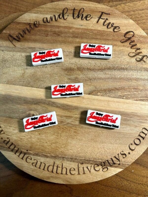 Five rectangular pins with red and black text reading "Lady Luscious Lips" displayed on a circular wooden board with the text "Annie and the Five Guys" around the edge.