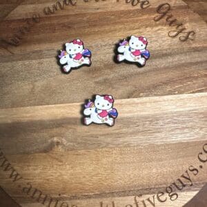 Three White HK riding a unicorn pins with pink bows, wings, and rainbow tails are positioned on a round wooden coaster featuring the text "Annie and the Five Guys" and a website URL.