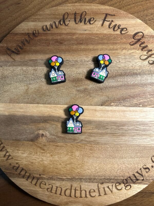 Three colorful Balloon house silicone focal beads are arranged on a wooden surface with the text "Annie and the Five Guys" engraved on it.