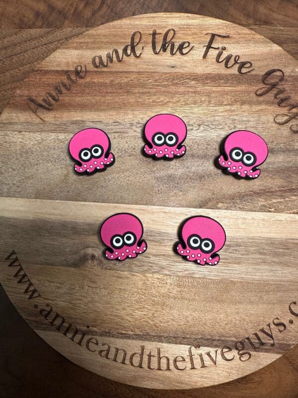 Five pink octopus-shaped magnets are arranged on a circular wooden board with the text "Annie and the Five Guys" and the website "www.annieandthefiveguys.com" engraved around the edge.