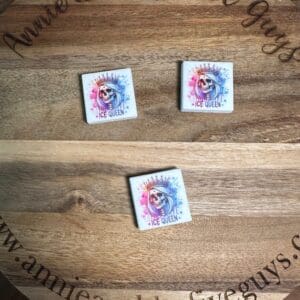 Three small square tiles with "Ice Queen" text and an image of a woman wearing a blue wig and crown are displayed on a wooden surface. The website "www.annieandthefiveguys.com" is partially visible.