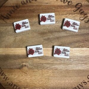 Five rectangular tiles with a flower design and text are arranged on a circular wooden board engraved with "www.annieandthefiveguys.com".