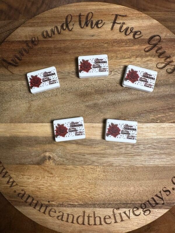 Five rectangular tiles with a flower design and text are arranged on a circular wooden board engraved with "www.annieandthefiveguys.com".