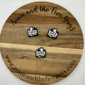 Wooden circular board engraved with "Annie and the Five Guys" and website link, displaying three square pins with the text "love & peace" and a dove illustration.