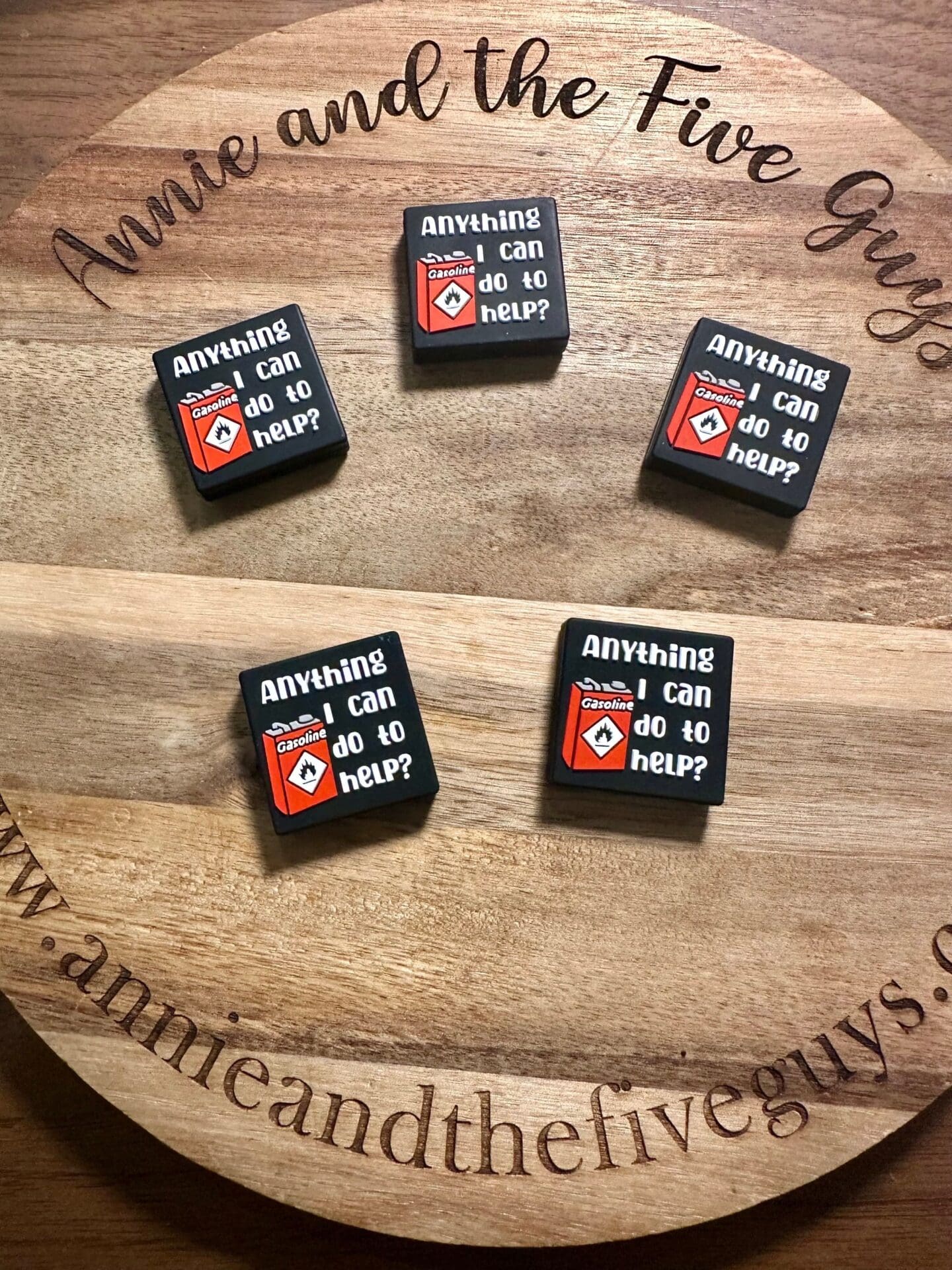 Five square pins display the phrase "Anything I can do to help?" with a red diamond logo on a wooden board that says "Annie and the Five Guys.