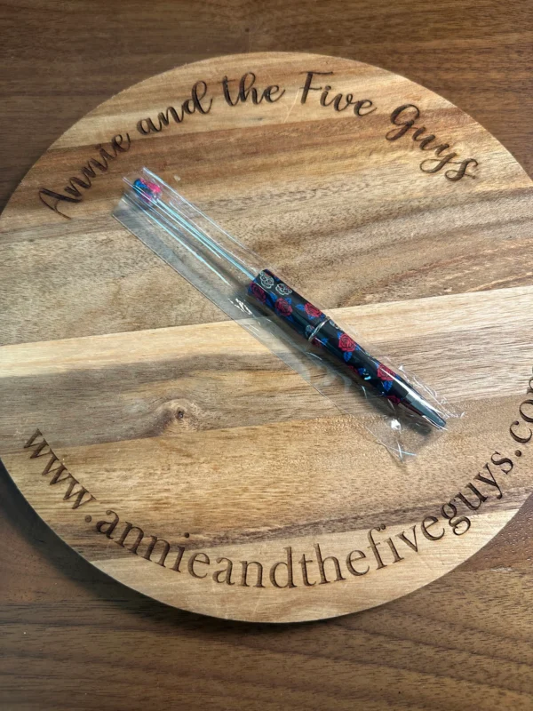 A clear-handled Printed Beadable pen with decorative designs rests across a circular wooden board. Text engraved on the board reads "annieandthefiveguys" along with the website "www.annieandthefiveguys.com".