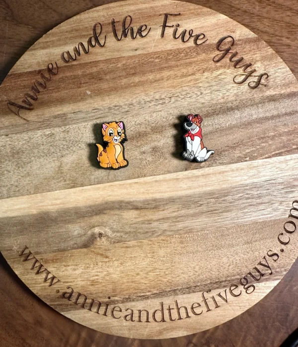 Two cat or dog silicone focal beads on a round wooden board that has the text "Annie and the Five Guys" and "www.annieandthefiveguys.com" engraved on it.