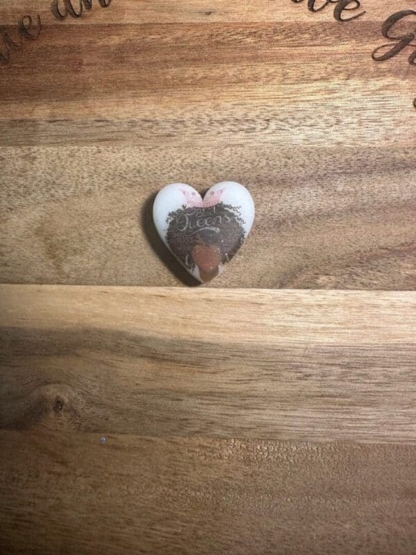 A heart-shaped magnet reads "Queens are born in January" with a small crown illustration on a wooden surface.