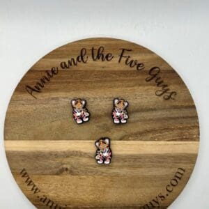 Three LF Tiger silicone focal beads are arranged on a wooden board with the text "Annie and the Five Guys" engraved on it. A website URL, "www.annieandthefiveguys.com," is also shown at the bottom of the board.