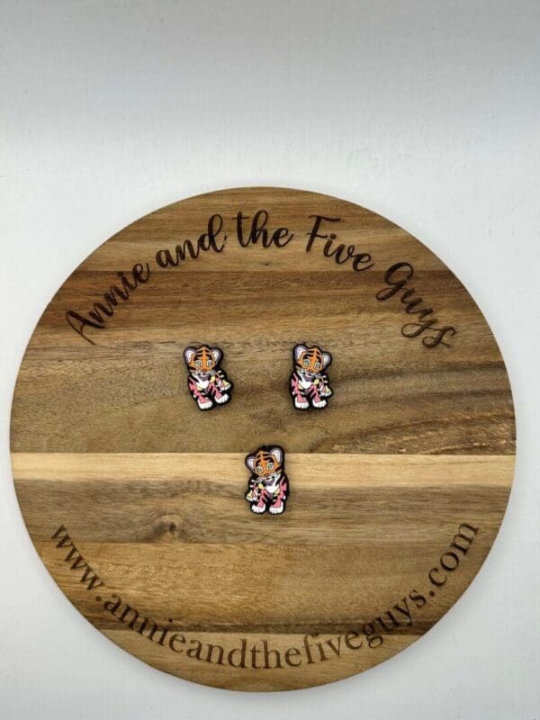 Three LF Tiger silicone focal beads are arranged on a wooden board with the text "Annie and the Five Guys" engraved on it. A website URL, "www.annieandthefiveguys.com," is also shown at the bottom of the board.