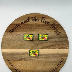 Round wooden plaque with the text "Annie and the Five Guys" engraved around the rim. Three colorful enamel pins with the text "Save Our Earth" are displayed in the center.