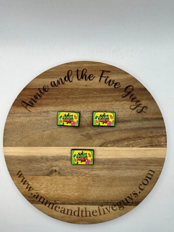 Round wooden plaque with the text "Annie and the Five Guys" engraved around the rim. Three colorful enamel pins with the text "Save Our Earth" are displayed in the center.