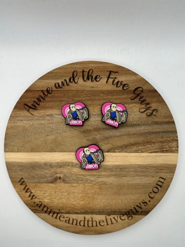 Three Jason silicone focal beads with a graphic of a character holding a sack and a heart are displayed on a round wooden board with the text "Annie and the Five Guys" engraved on it.