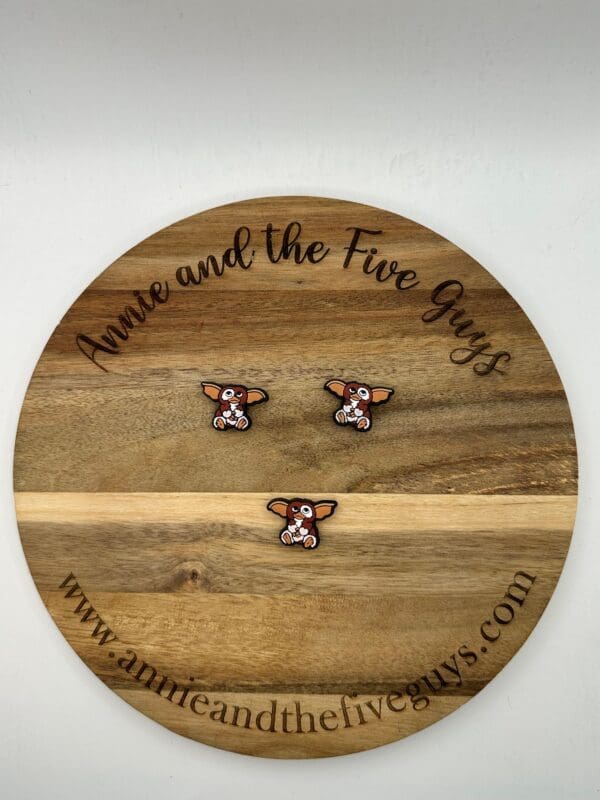 Wooden round board labeled "Annie and the Five Guys" displaying three small pins featuring a character with large ears and expressive eyes at different positions.