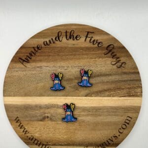 A round wooden board with the text "Annie and the Five Guys" displays three colorful pins shaped like blue slugs with butterfly wings on their heads. Website URL is visible at the bottom of the board.