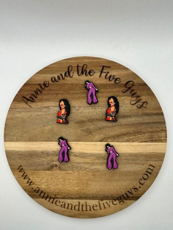 Five Selena silicone focal beads featuring a woman in red and purple attire are displayed on a round wooden board with the text "Annie and the Five Guys" and a website URL.