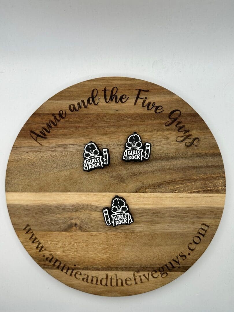 Three "Girls Rock" pins displayed on a round wooden board with the text "Annie and the Five Guys" and a website URL around the edge.