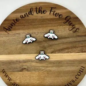 A circular wooden board with three small pins on it, each depicting a panda with wings. The board is engraved with the text "Cinnamon bear silicone focal bead" and the website "www.annieandthefiveguys.com".