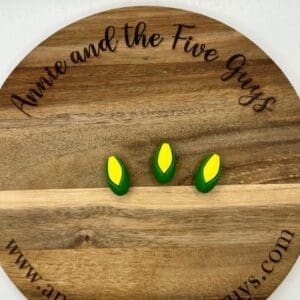 A round wooden board with three small ear of corn magnets. The board is labeled "Annie and the Five Guys" with the website "www.annieandthefiveguys.com".