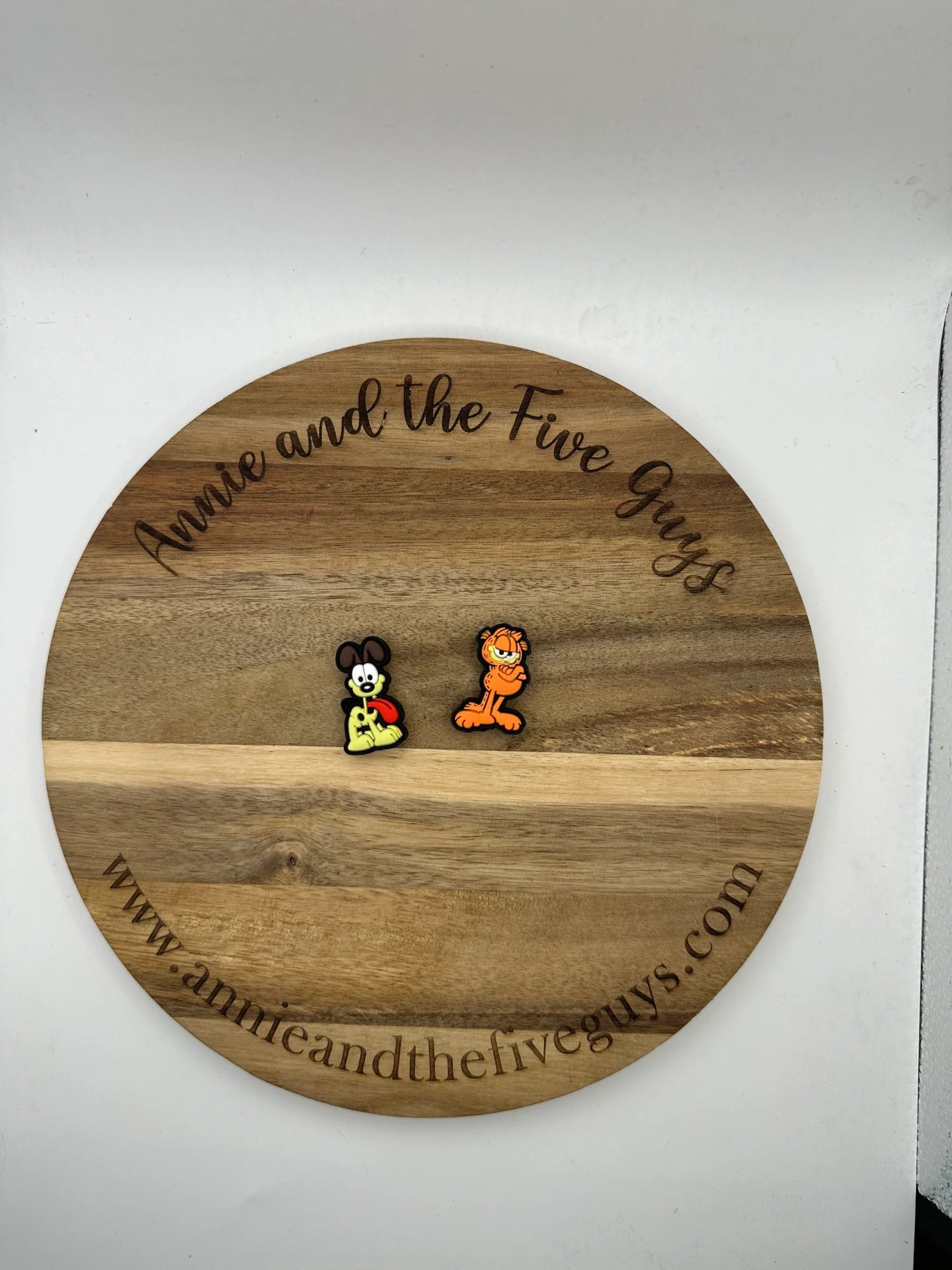 A wooden board with text "Orange Cat and Yellow Dog Silicone Focal Bead" circularly engraved on the edge, featuring two small cartoon character pins.