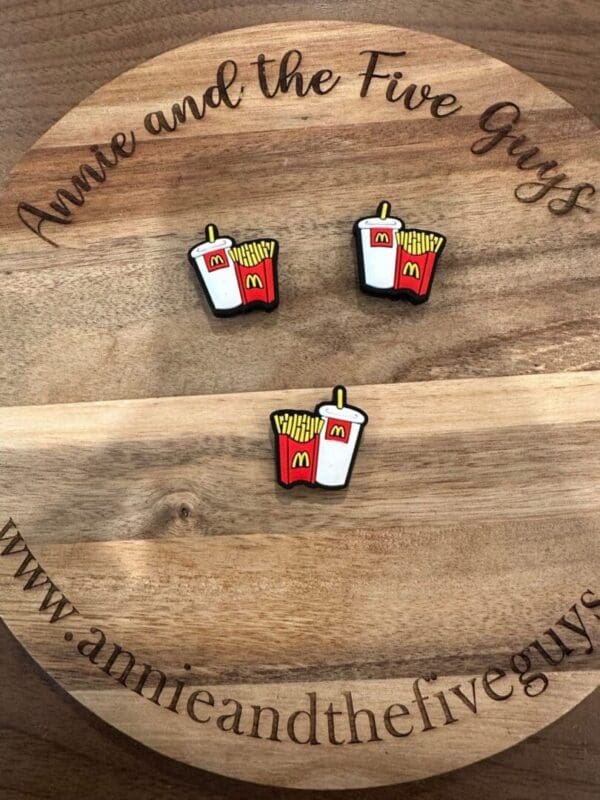 Three Fast food fries silicone focal beads depicting French fries and a soda with McDonald's logos are displayed on a wooden plaque that reads "Annie and the Five Guys" and includes a related website URL.