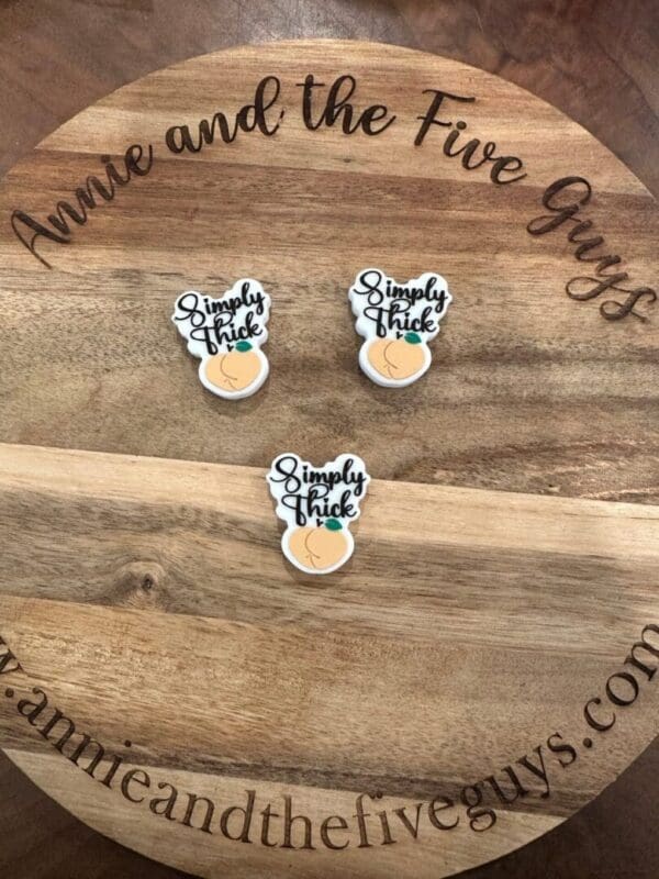 Three "Simply thick silicone focal bead" branded items are placed on a wooden surface featuring the website "annieandthefiveguys.com" and the text "Annie and the Five Guys" around the edge.