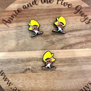 Three cartoon character pins with yellow hair and white outfits are displayed on a round wooden surface with the text "Annie and the Five Guys" and a web address.