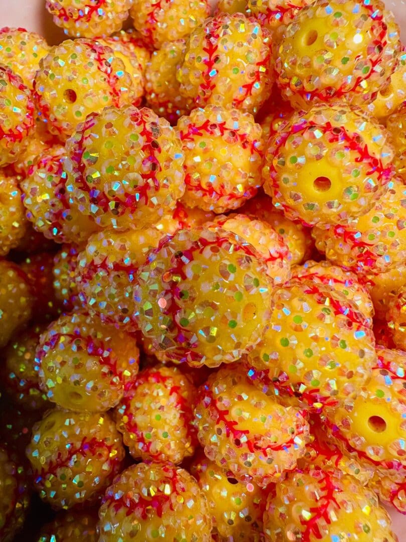 A pile of small, yellow beaded balls decorated with iridescent sequins and red thread detailing.