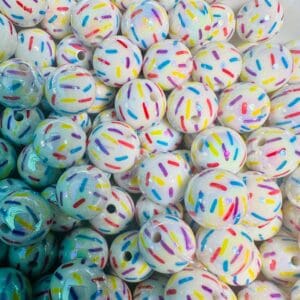 A pile of white round beads decorated with colorful sprinkles-like patterns in red, blue, yellow, and purple.