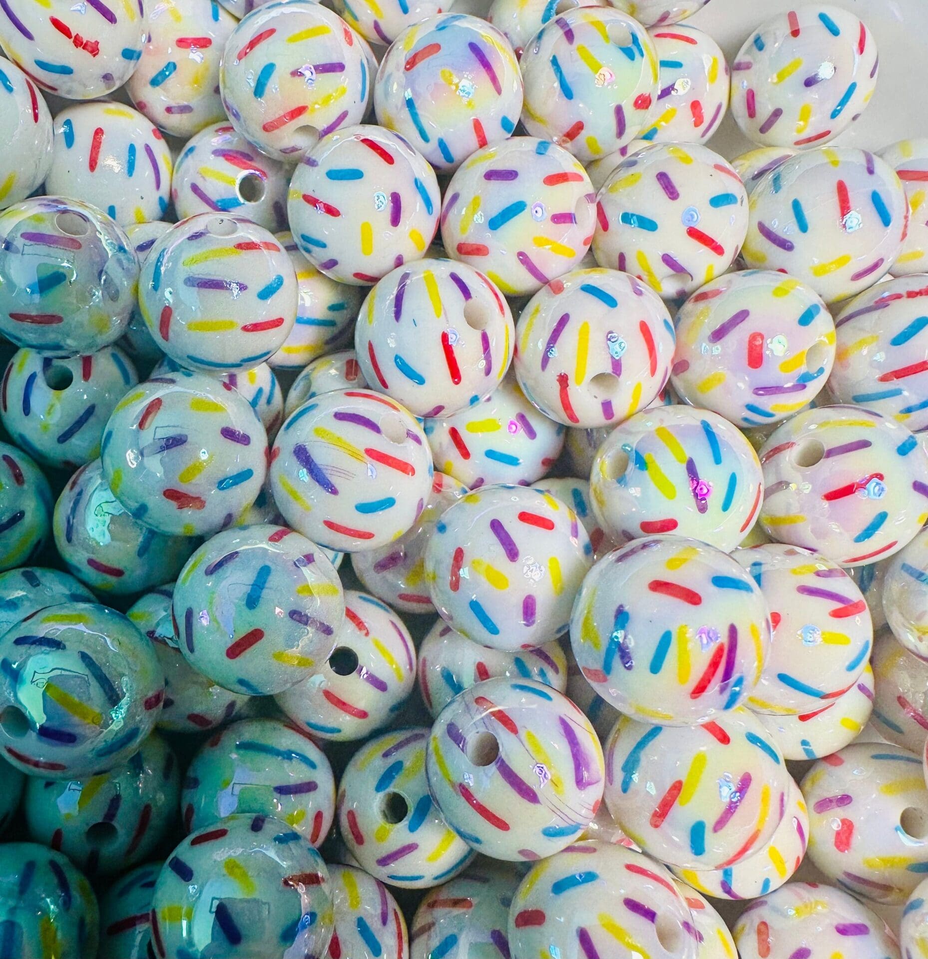 A pile of white round beads decorated with colorful sprinkles-like patterns in red, blue, yellow, and purple.