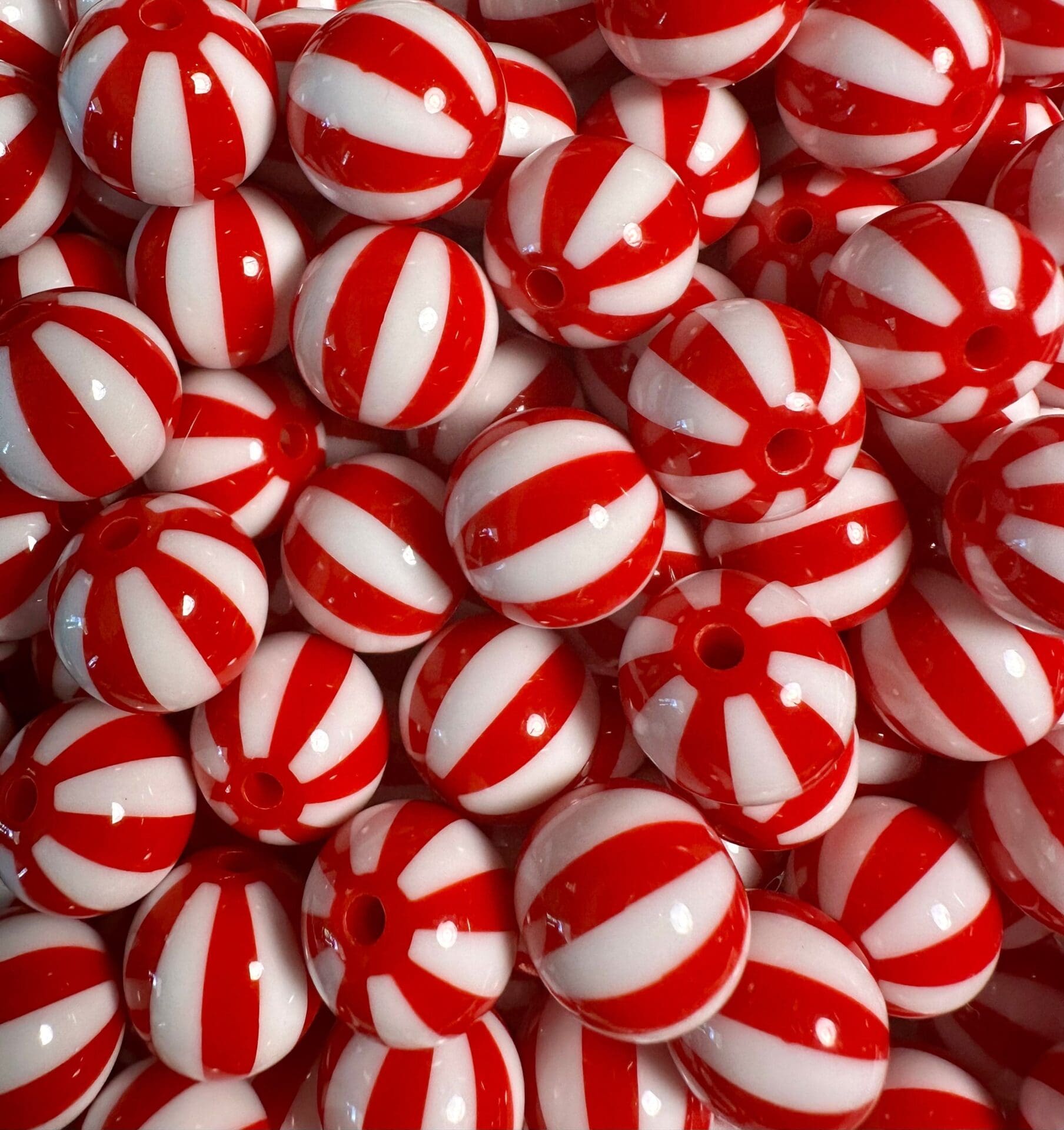 A close-up of numerous red and white striped round beads, resembling peppermint candies, piled together.