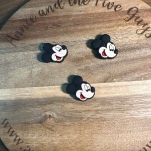 Three Mickey Mouse face stickers on a round wooden board with the text "Annie and the Five Guys" engraved on it.