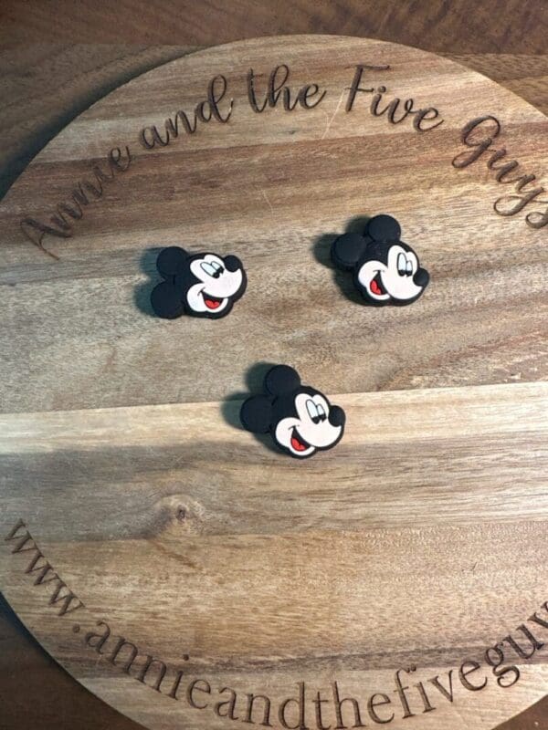 Three Mickey Mouse face stickers on a round wooden board with the text "Annie and the Five Guys" engraved on it.