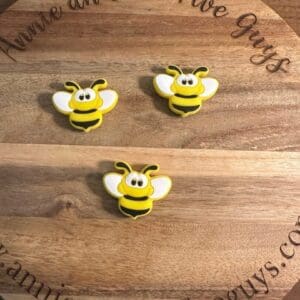 Three yellow and black bee-shaped magnets are arranged on a round wooden board with the text "Annie and the Five Guys" engraved around the edge.