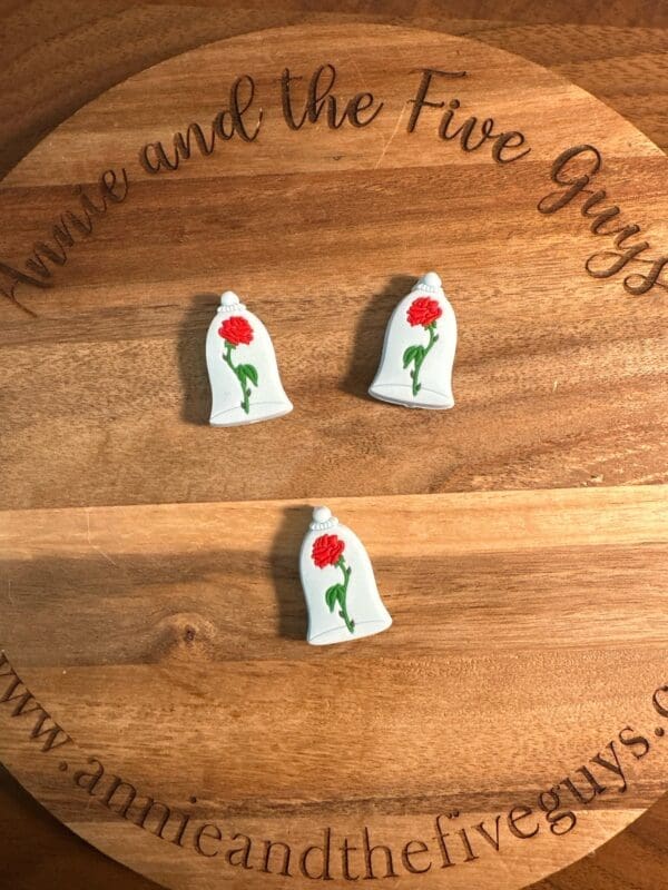 Three Rose in a vase silicone focal beads are placed on a wooden round board with the text "www.annieandthefiveguys.com" and "Annie and the Five Guys" inscribed on it.