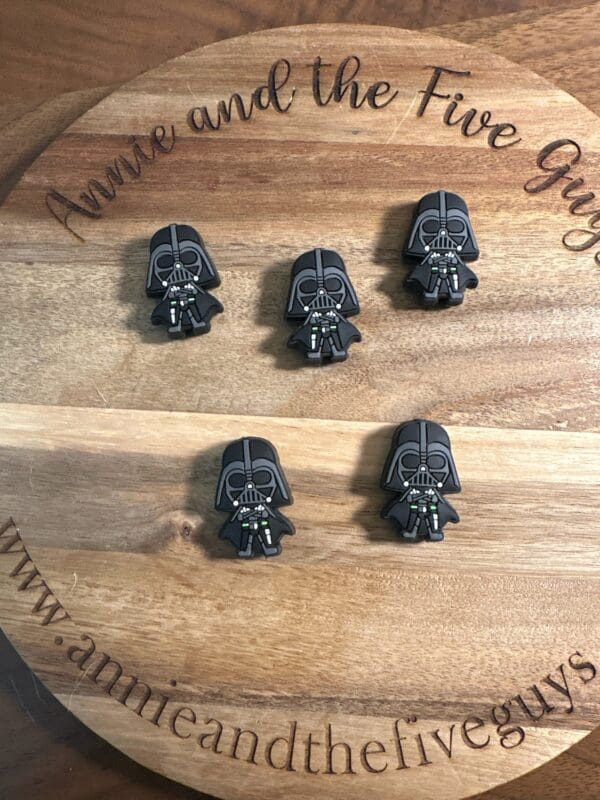 A wooden board with the text "Annie and the Five Guys" displays five small plastic figures resembling a Dark side Focal Bead.