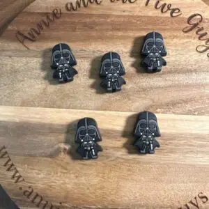 A wooden board with the text "Annie and the Five Guys" displays five small plastic figures resembling a Dark side Focal Bead.