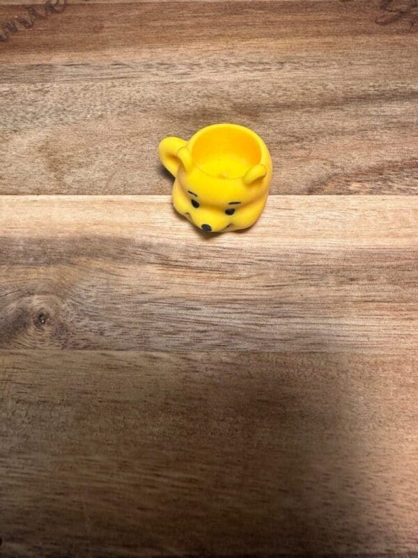 A small yellow Sanrio cups resin bead shaped like a bear's head sits on a wooden surface.