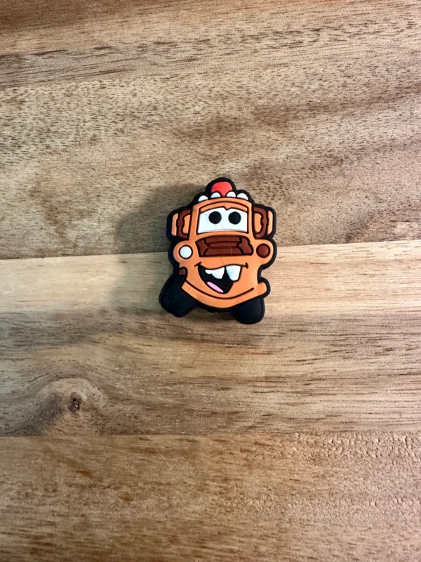 A small cartoon truck or car silicone focal bead with a big toothy smile and googly eyes lies on a wooden surface.