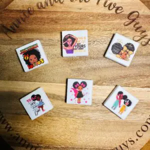 Six African American girl, women, Juneteenth silicone focal beads are displayed on a wooden surface with the website "annieandthefiveguys.com" faintly visible in the background.