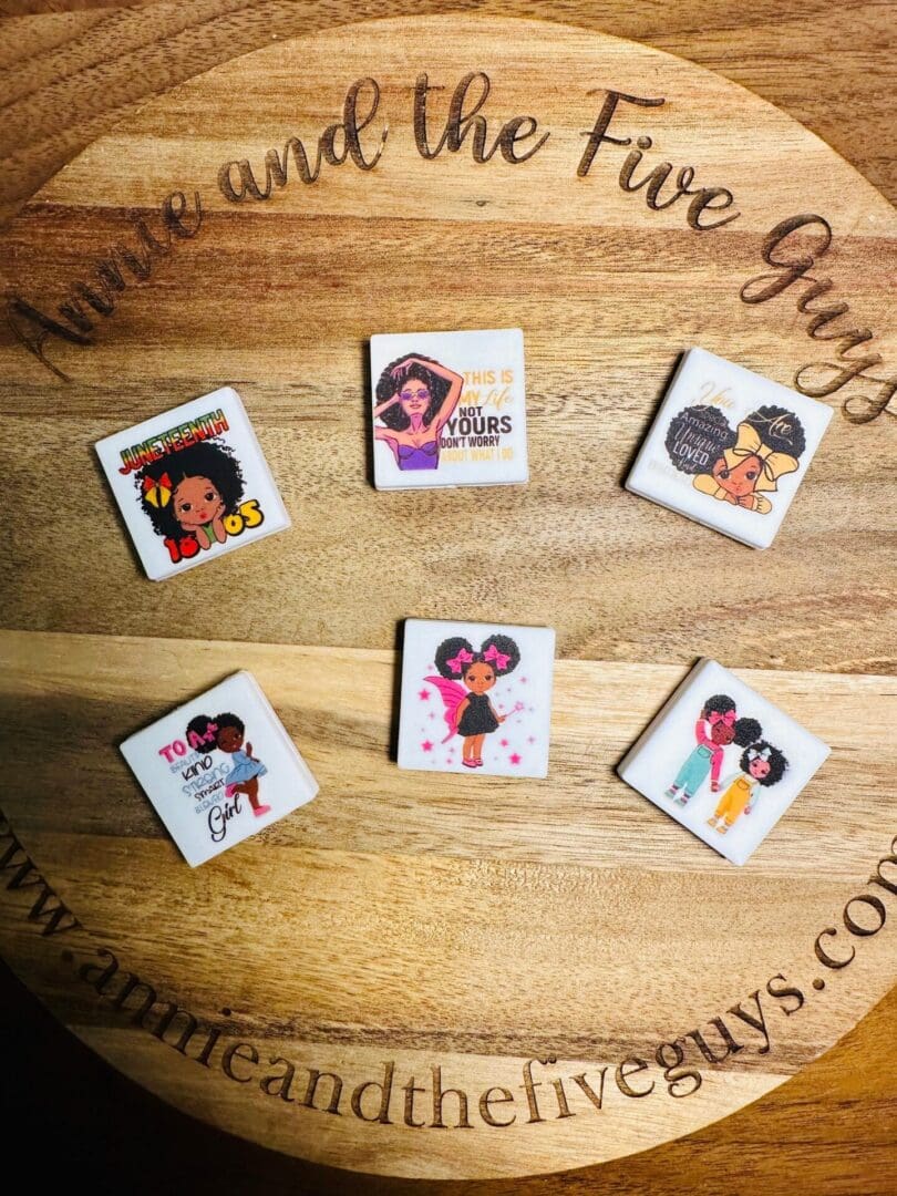 Six African American girl, women, Juneteenth silicone focal beads are displayed on a wooden surface with the website "annieandthefiveguys.com" faintly visible in the background.