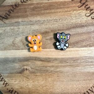 Two Cat and mouse silicone focal beads, one of a yellow mouse and the other a gray cat, placed on a circular wooden surface with text "Annie and the Five Guys" around the edge.