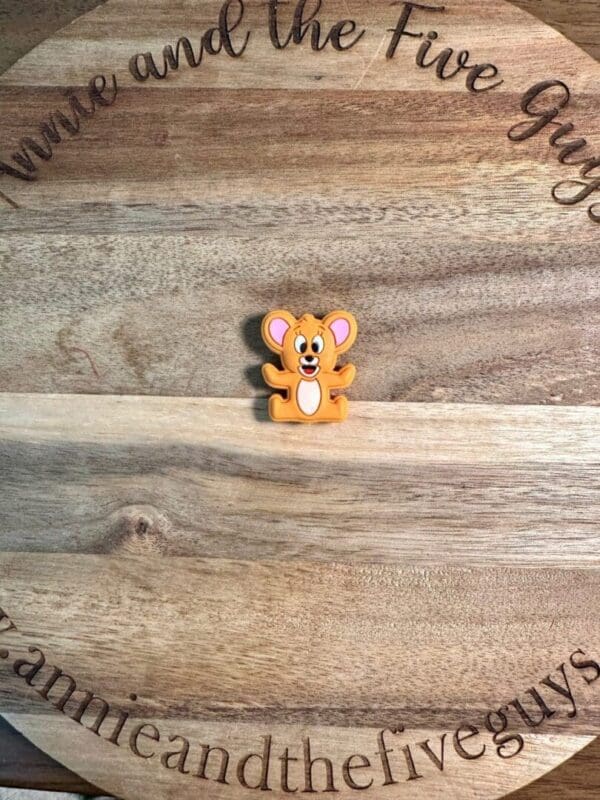 A Cat and Mouse Silicone Focal Bead with a smiling face placed on a wooden board with engraved text reading "www.annieandthefiveguys.com.