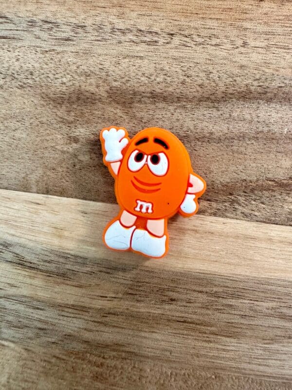 A candy silicone focal bead with white gloves and shoes, standing on a wooden surface and raising one hand.