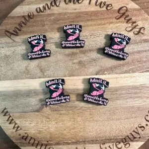 A wooden board with the text "Annie and the Five Guys" displays six Flamingo, funny silicone focal beads that read "Admit it. You would be boring without me." with a pink design. The website amyandthefiveguys.com is also visible.