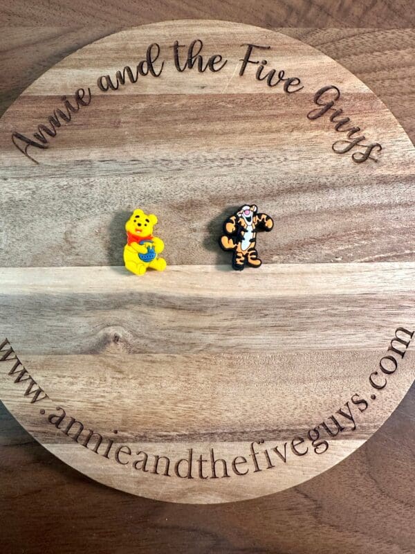 Two character figurines, one of a yellow bear and one of a tiger, are displayed on a circular wooden board with the text "Honey bear or tiger silicone focal bead" and a website URL.