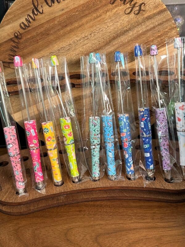 A row of colorful, patterned Beadable pens with nursing, doctor, healthcare print wrapped in plastic packaging displayed on a wooden surface.