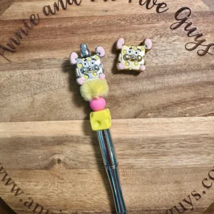 A Mouse cheese bead with a fluffy, decorated topper resembling a mouse and a square-shaped mouse-themed charm placed on a wooden surface with the engraved text "Annie and the Five Guys".