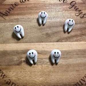 Wooden board with 'Annie and the Five Guys' text, displaying five 3D teeth with pink cheeks arranged in a circle.